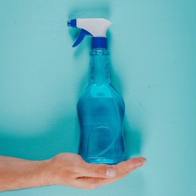 Top view man holding cleaning solution on cyan blue background. vertical